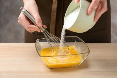 Woman adding sugar to whisked eggs at wooden table, closeup