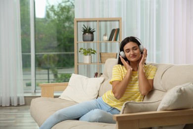 Young woman listening to music on sofa at home, space for text