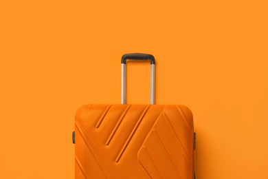 Stylish bright suitcase on orange background, top view