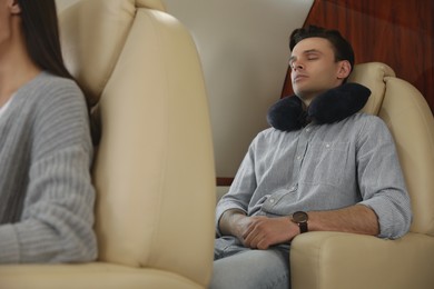 Young man with travel pillow sleeping in airplane during flight