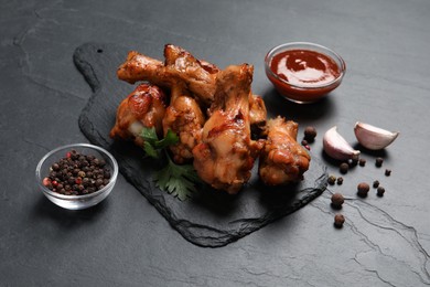 Delicious fried chicken wings, tomato sauce and bowl of pepper peas on black table