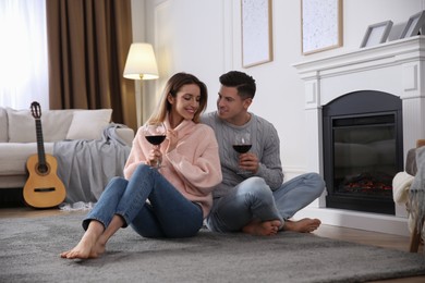 Happy couple with glasses of wine resting near fireplace at home