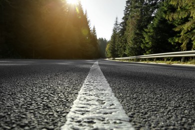 Closeup view of asphalt road surrounded by forest on sunny day