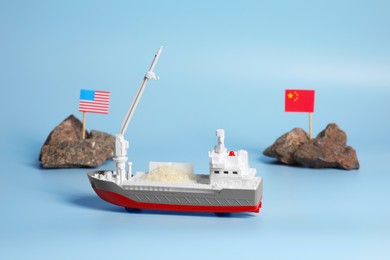 Toy cargo vessel, stones with American and Chinese flags on light blue background. Export concept