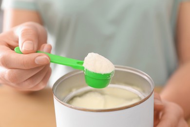 Woman with powdered infant formula at table, closeup. Preparing baby milk