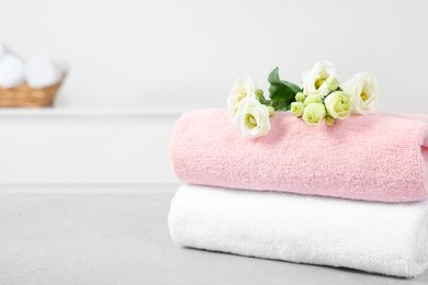 Soft folded towels and eustoma flowers on white table, space for text