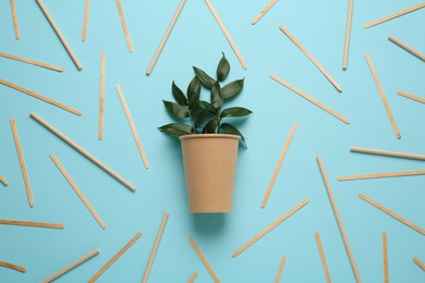Paper cup with green twigs surrounded by bamboo straws and sticks on turquoise background, flat lay. Eco friendly lifestyle