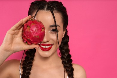 Young woman with fresh pitahaya on pink background, space for text. Exotic fruit