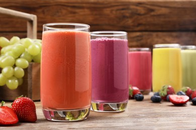Glasses with different tasty smoothies and ingredients on wooden table, closeup