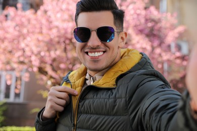 Happy man with sunglasses taking selfie outdoors on spring day
