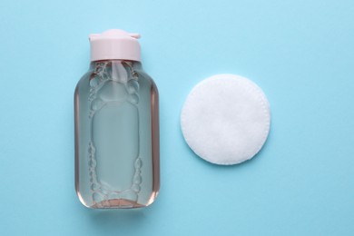 Micellar water and cotton pad on light blue background, flat lay