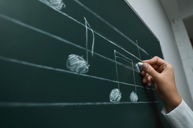 Teacher writing music notes with chalk on greenboard, closeup
