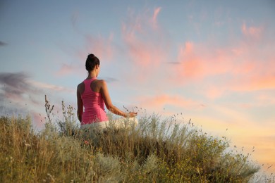 Woman meditating in meadow, back view. Space for text