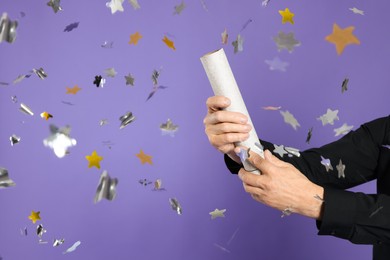 Photo of Man blowing up party popper on purple background, closeup