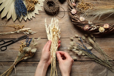 Florist making bouquet of dried flowers at wooden table, top view