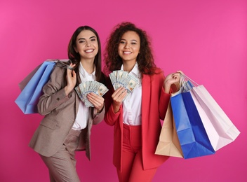 Young women with money and shopping bags on color background