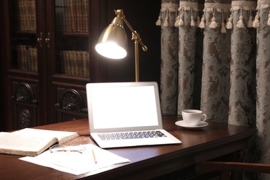 Laptop, book and papers on wooden table in library reading room