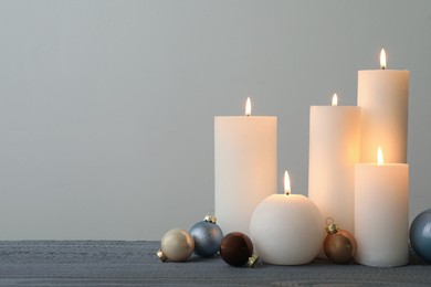 Photo of Burning candles and Christmas baubles on grey wooden table. Space for text