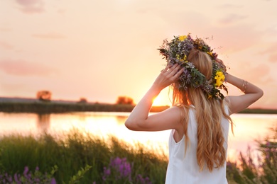 Young woman wearing wreath made of beautiful flowers outdoors at sunset