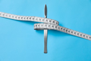 Scalpel and measuring tape on light blue background, top view. Weight loss surgery