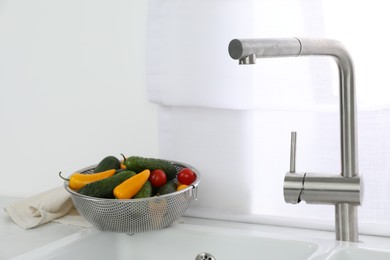 Photo of Modern sink with water tap and fresh vegetables near window in kitchen