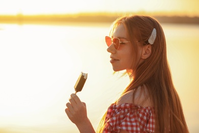 Beautiful young woman with ice cream outdoors at sunset