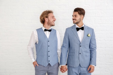 Happy newlywed gay couple in suits against white wall