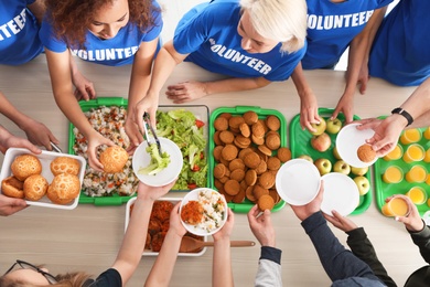 Volunteers serving food to poor people at table, top view