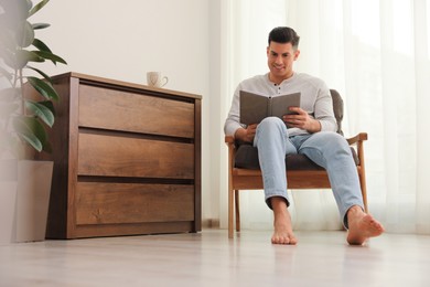 Man with book sitting in armchair at home. Floor heating system