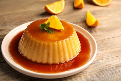 Photo of Delicious pudding with caramel, orange and mint on wooden table