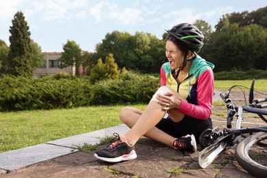 Young woman with injured knee near bicycle outdoors, space for text