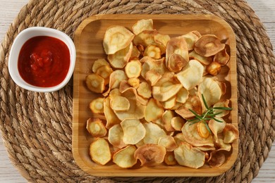 Photo of Tasty homemade parsnip chips with sauce on white wooden table, top view