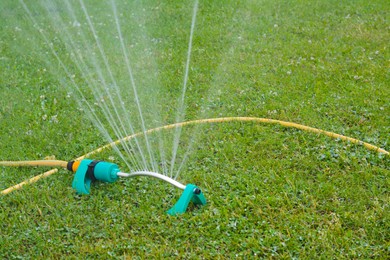 Photo of Automatic sprinkler watering green grass on lawn outdoors