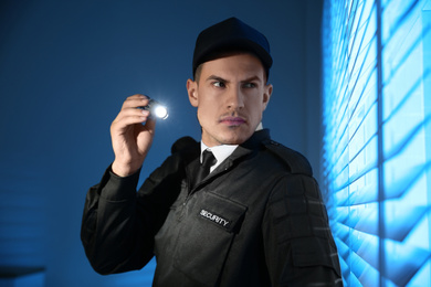 Professional security guard with flashlight near window in dark room