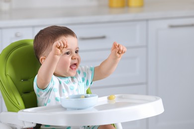 Cute little baby eating healthy food in high chair at home, space for text