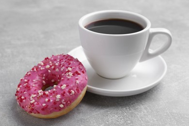 Photo of Tasty frosted donut and cup of coffee on light grey table