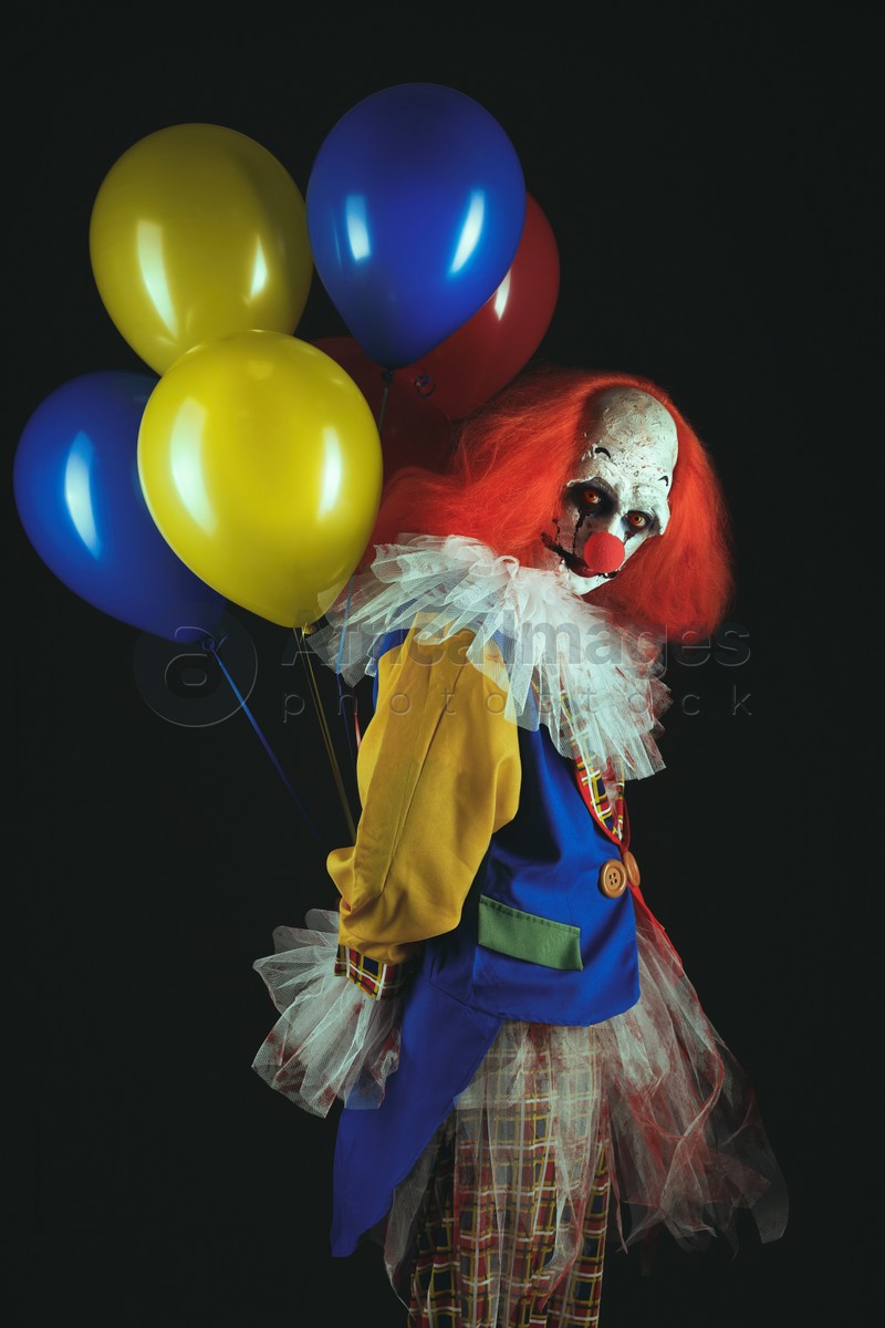 Photo of Terrifying clown with air balloons on black background. Halloween party costume