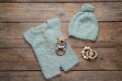 Baby toys, knitted romper and hat on wooden background, flat lay