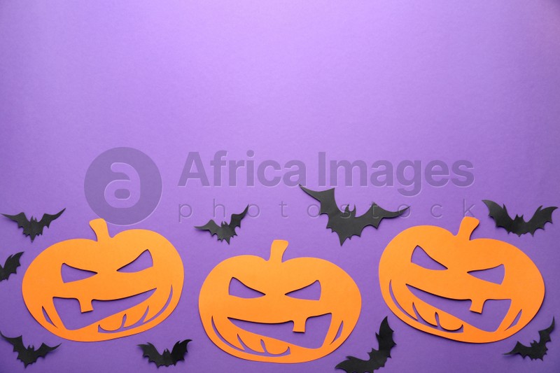 Flat lay composition with spooky paper pumpkins and bats on purple background, space for text. Halloween decor