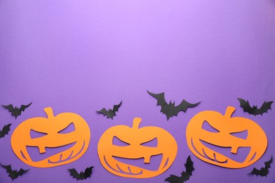 Flat lay composition with spooky paper pumpkins and bats on purple background, space for text. Halloween decor