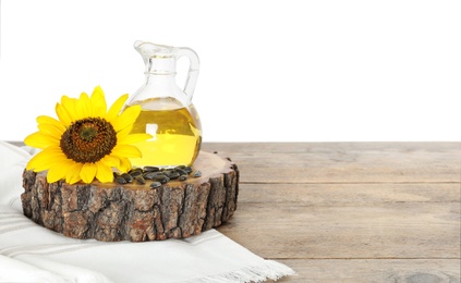 Sunflower, jug of oil and seeds on wooden table against white background, space for text