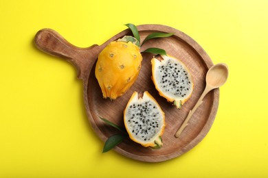 Photo of Wooden platter with fresh dragon fruits (pitahaya) and spoon on yellow background, top view