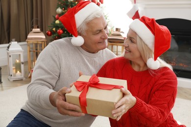 Happy mature couple in Santa hats with gift box at home. Christmas celebration
