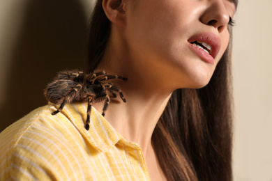 Photo of Young woman with tarantula on beige background, closeup. Arachnophobia (fear of spiders)