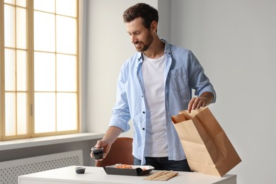 Photo of Man unpacking his order from sushi restaurant at table in room