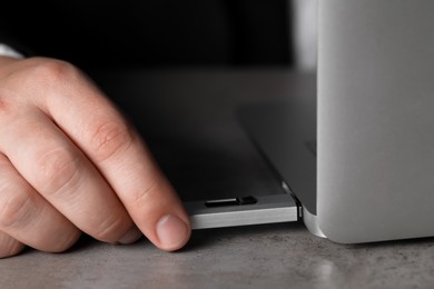 Man connecting usb flash drive to laptop at grey table, closeup