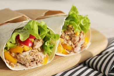 Photo of Delicious tortilla wraps with tuna on wooden board, closeup. Space for text