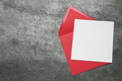 Envelope with blank paper card on grey table, top view. Space for text
