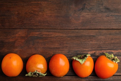 Delicious fresh persimmons on wooden table, flat lay. Space for text