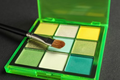 Photo of Colorful eyeshadow palette with brush on dark background, closeup